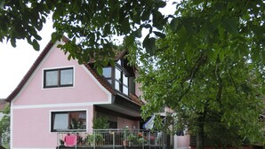 A two-story pink house with a balcony, a small garden, and a basketball hoop. - Ferienwohnung Singer (Schnaittach)