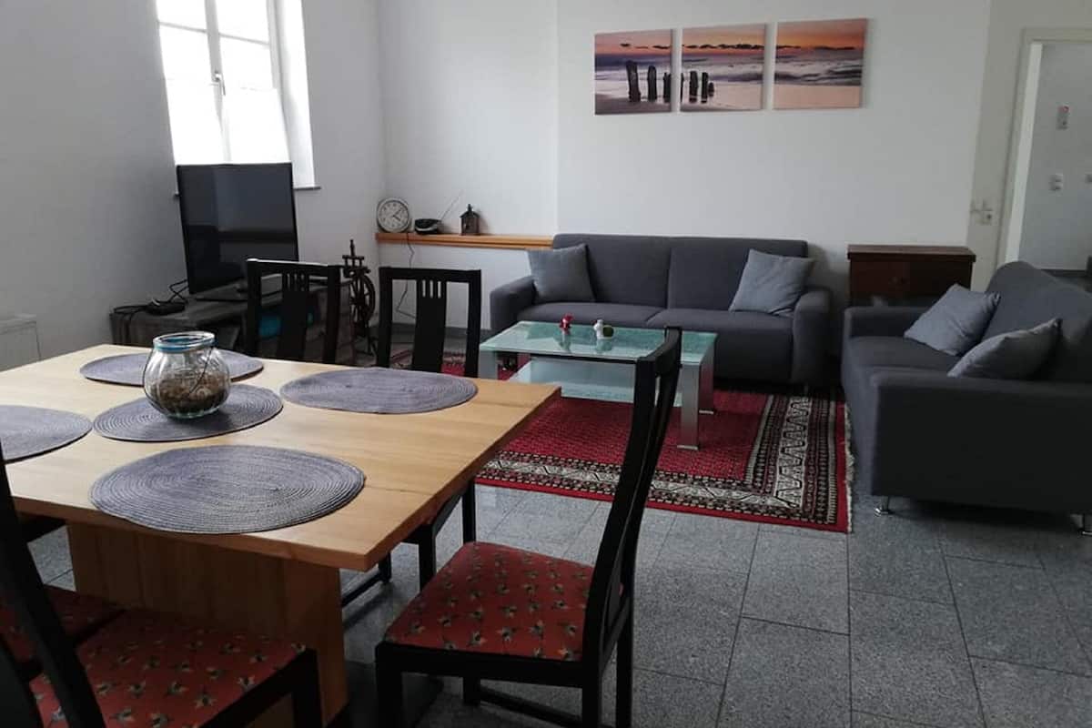 Un salon avec une table à manger en bois, des chaises rouges, un canapé gris et une table basse en verre.