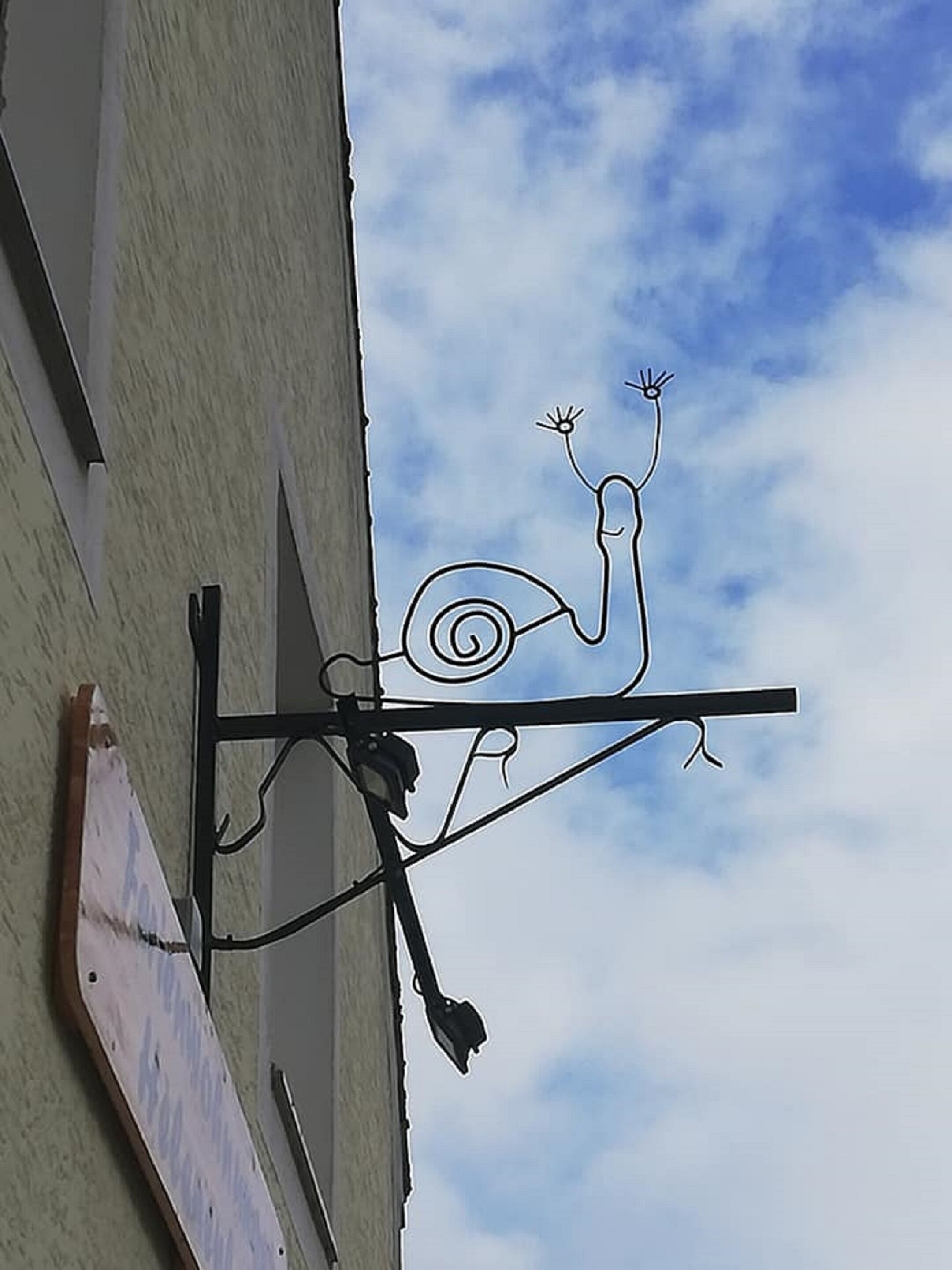 A metal sign with a snail design, attached to a building's exterior.