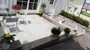 Un patio couvert avec une table et des chaises en verre, des plantes en pot et un petit espace jardin agrémenté d’un sentier.