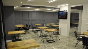A modern dining area with multiple wooden tables and black wireframe chairs, a flat-screen TV mounted on the wall, and patterned floor tiles. - Oropa Butik Hotel (Eynesil)