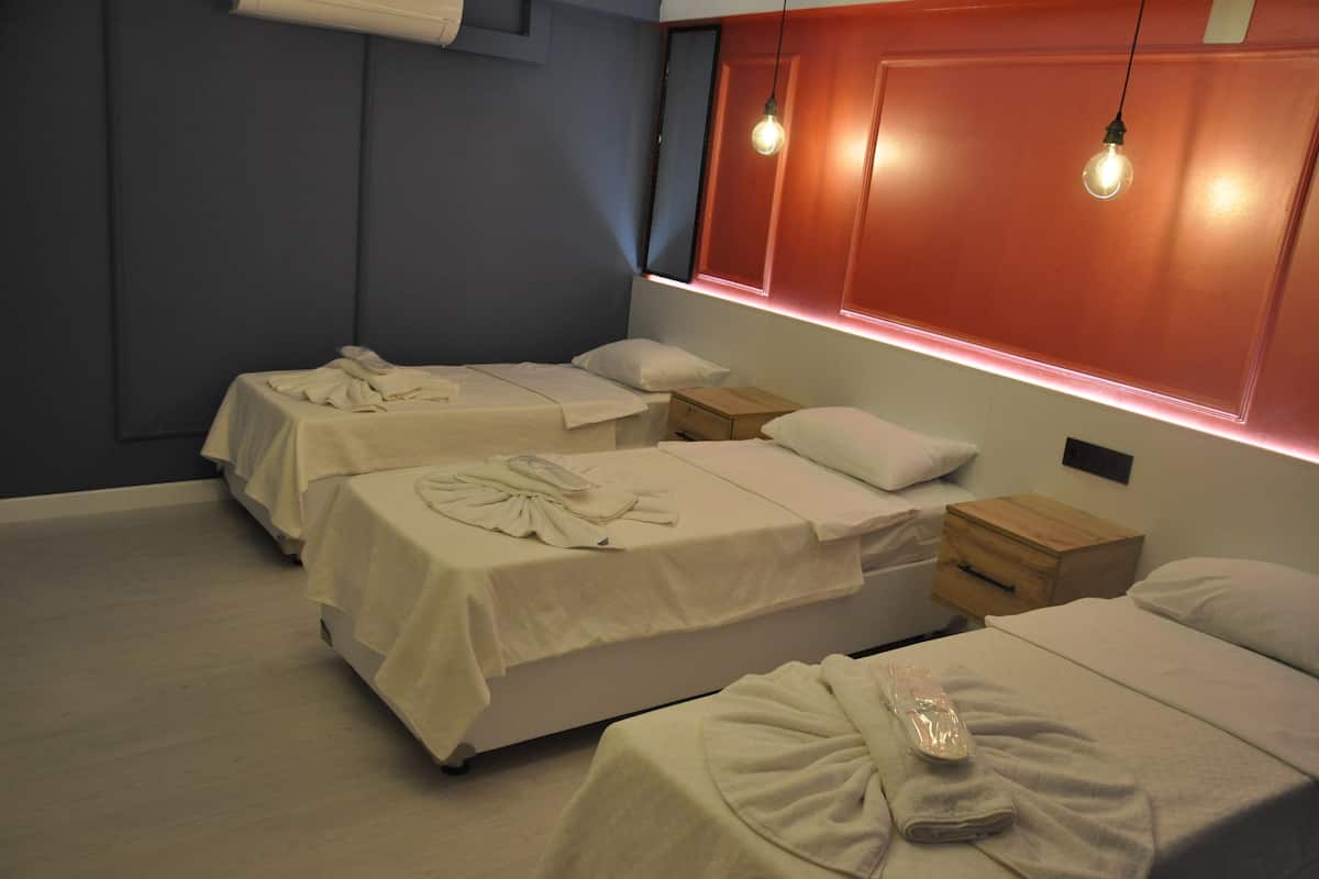 A hotel room with three beds, each with white linens and pillows, a wooden nightstand, and a wall-mounted light fixture.