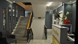 A reception area with a marble floor, a staircase with wooden handrails, and a reception desk with a sign. - Oropa Butik Hotel (Eynesil)