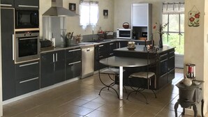 A spacious kitchen with modern appliances, a dining area, and a view of the outdoors. - Maison 190m2 Chambres Climatisées, Piscine Privée, Proche Village (Velleron)