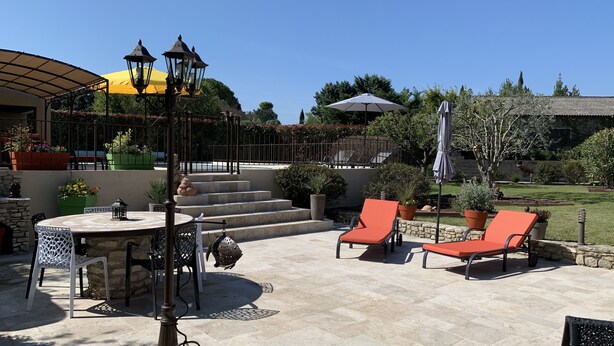 An outdoor patio with a round table, two orange lounge chairs, and a pergola with yellow and black lanterns. - Maison 190m2 Chambres Climatisées, Piscine Privée, Proche Village (Velleron)