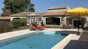 A swimming pool with a tiled deck, two red lounge chairs, and a yellow umbrella. - Maison 190m2 Chambres Climatisées, Piscine Privée, Proche Village (Velleron)