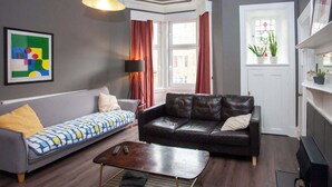 A living room with a grey sofa, a black leather sofa, a coffee table, a floor lamp, a painting, and a window with curtains.