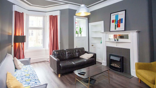 A living room with a leather sofa, a yellow armchair, a coffee table, a fireplace, and a large window with curtains.