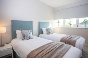 Una habitación de hotel con dos camas, una mesita de noche, una ventana con persianas y una lámpara.