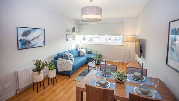 A modern living room with a blue sofa, dining table set, and potted plants. - Stylish 2-Bed Apartment Near Glasgow Green (Glasgow City)