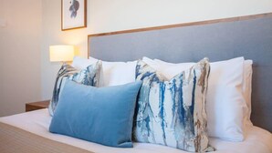 A neatly made bed with a blue pillow and patterned pillows, a bedside lamp, and a framed picture on the wall. - Stylish 2-Bed Apartment Near Glasgow Green (Glasgow City)