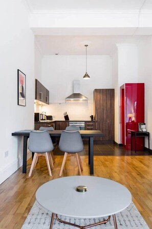 A modern kitchen with a dining area, featuring a round table, two chairs, and a red cabinet.