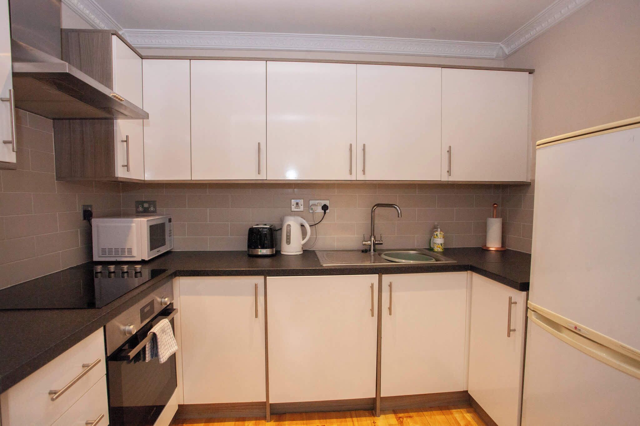 A compact kitchen with white cabinets, a microwave, a kettle, and a sink.