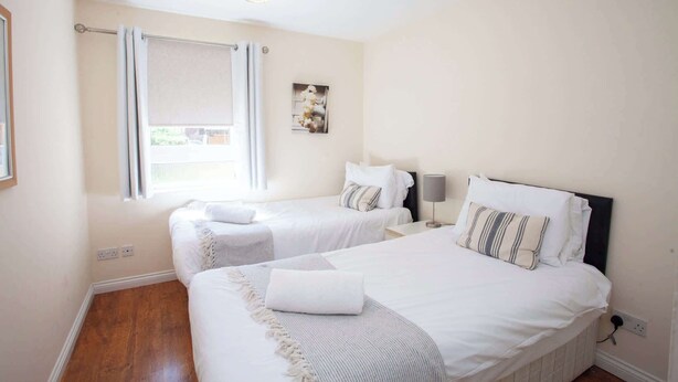 A hotel room with two beds, a window with curtains, a wall-mounted picture, and a hanging light fixture. - Homely Flat close to Centre with Free Parking! (Glasgow)