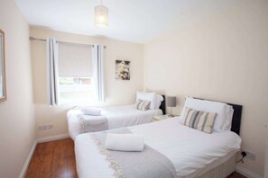 A hotel room with two beds, a window with curtains, a wall-mounted picture, and a hanging light fixture. - Homely Flat close to Centre with Free Parking! (Glasgow)