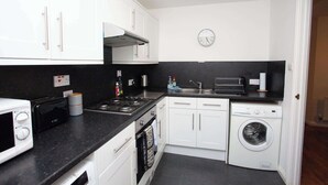 A compact kitchen with white cabinets, a microwave, a stove, a sink, and a washing machine. - Homely Flat close to Centre with Free Parking! (Glasgow)