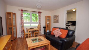 A living room with a black leather sofa, a wooden coffee table, a dining table with chairs, and a kitchen visible through an open door. - Homely Flat close to Centre with Free Parking! (Glasgow)
