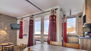 Ett modernt rum med ett matbord i trä, röda gardiner, en tv och utsikt över byggnaderna utanför.