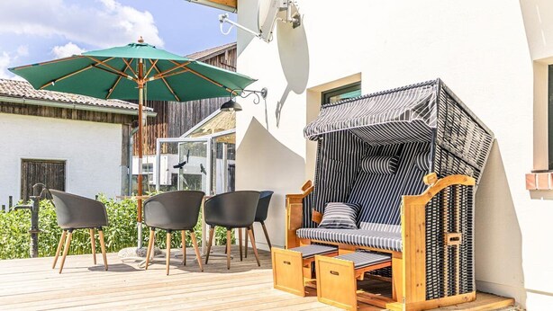 A wooden deck with a seating area, including a cushioned bench with a striped pattern and a green umbrella. - Peter-Anderl-Hof (Pfreimd)