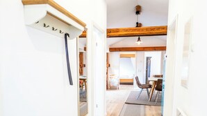 A hallway with a wooden floor, a white radiator, and a rug leading to a dining area with chairs and a table. - Peter-Anderl-Hof (Pfreimd)