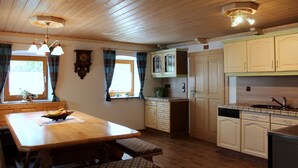 A wooden-paneled kitchen with a dining table, benches, and a clock on the wall. - Woidhaisl (Lam)