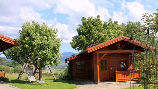 A wooden cabin with a porch, surrounded by lush greenery and a clear sky. - Woidhaisl (Lam)