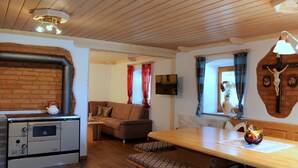 A cozy living room with a fireplace, a sofa, a dining table with a bowl of fruit, and a television mounted on the wall. - Woidhaisl (Lam)