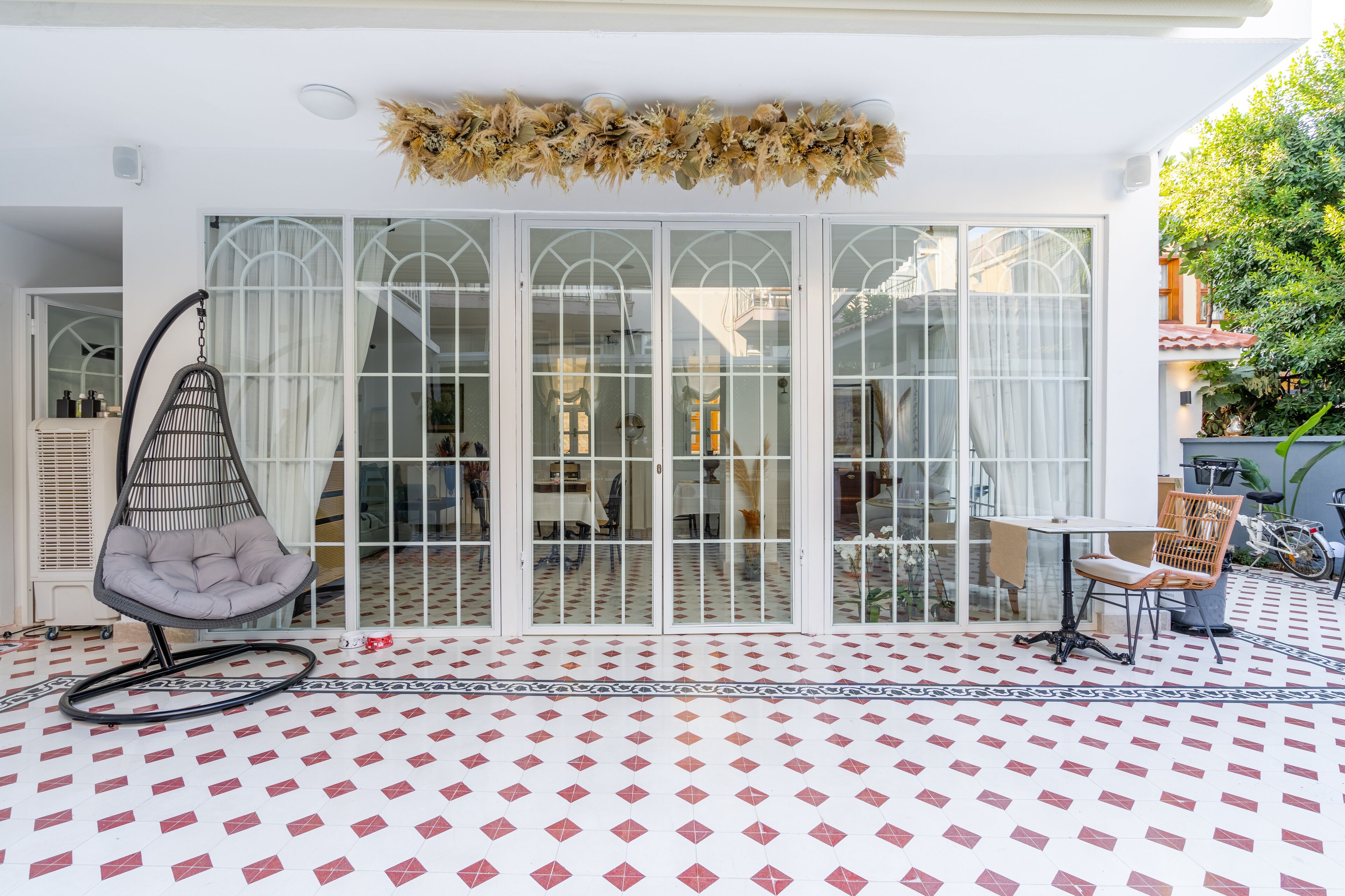 A patio with a patterned floor, a hanging chair, a table with chairs, and a decorative plant arrangement.