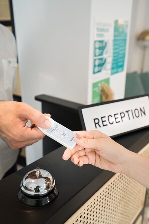 A hand receiving a card from another hand at a reception desk with a sign labeled "RECEPTION".