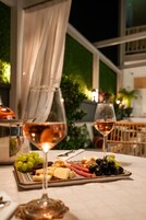 A table with a cheese platter, grapes, and wine glasses, set in a well-lit indoor area with a view of greenery outside.