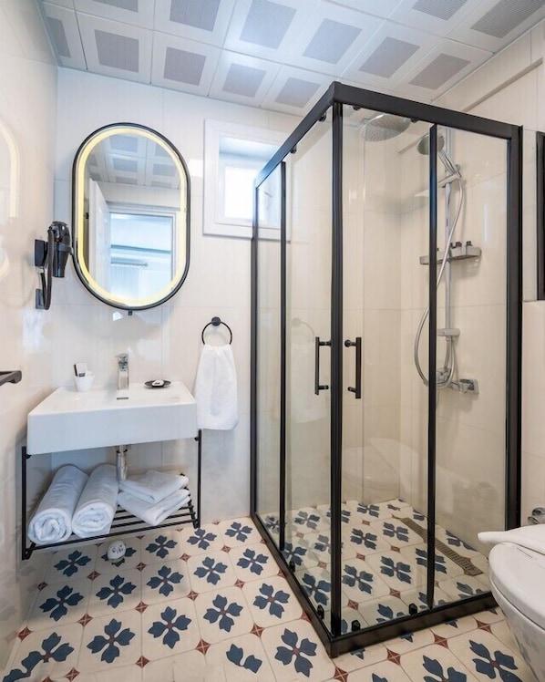 A bathroom with a glass-enclosed shower, a white sink with a mirror, and patterned floor tiles. - Kiana Kaleici (Antalya)