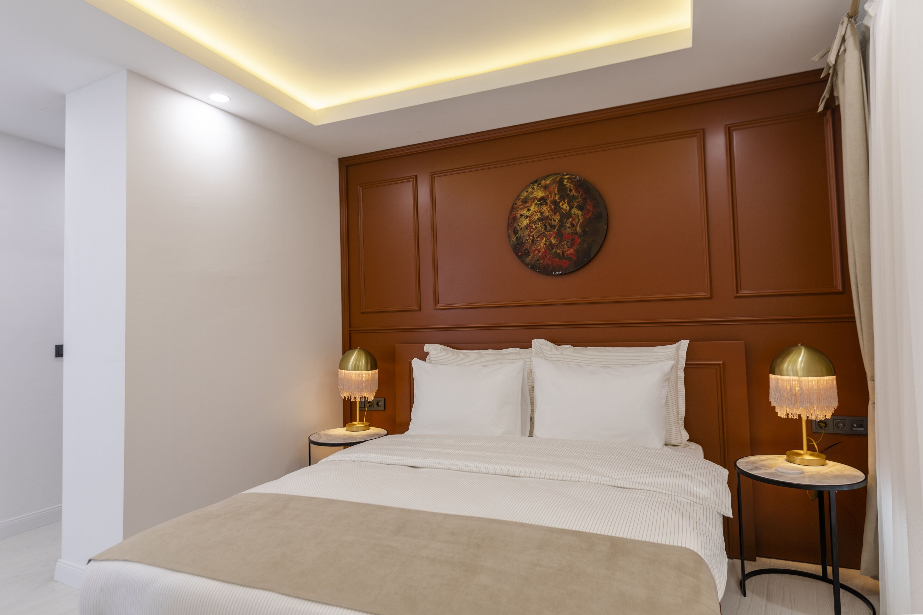 A hotel room with a large bed, two bedside tables, a round artwork on the headboard, and a modern ceiling design.