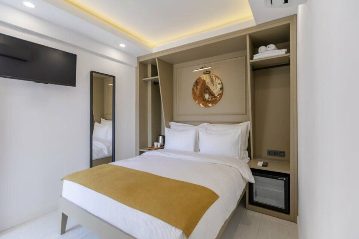 Ein modernes Hotelzimmer mit einem großen Bett, einem flachbildfernseher an der Wand, einem eingebauten Kleiderschrank und einem kleinen Kühlschrank.