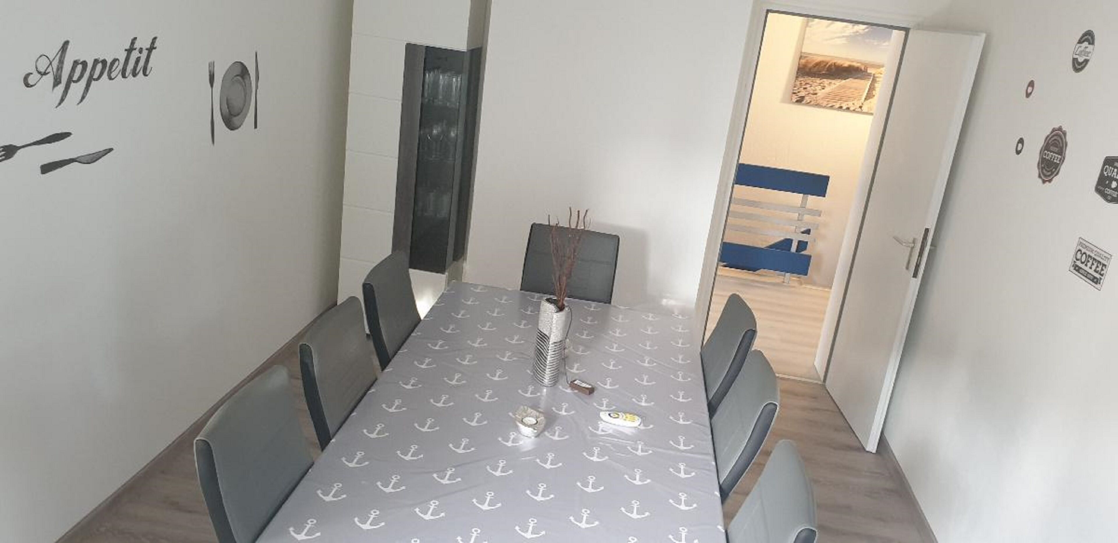 Un coin repas avec une table recouverte d’un motif décoratif, des chaises et une porte donnant sur une autre pièce.