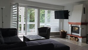 A living room with a sofa, armchair, and a fireplace. - Ferienwohnung Quednau (Grafenau)