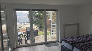 A bedroom with a bed, a desk, and a view through a sliding glass door to an outdoor area with a table and chairs. - Ferienwohnung Quednau (Grafenau)