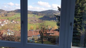 A view through a window of a rural landscape with houses, trees, and hills. - Ferienwohnung Quednau (Grafenau)