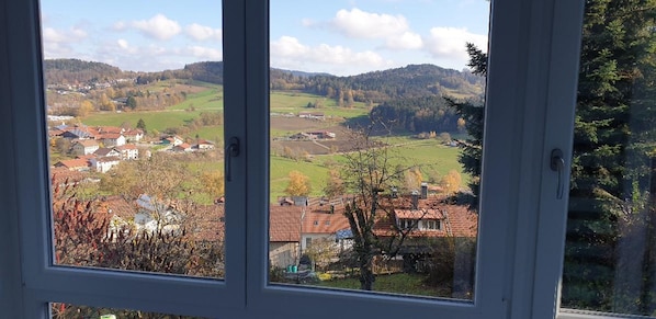A view through a window of a rural landscape with houses, trees, and hills.