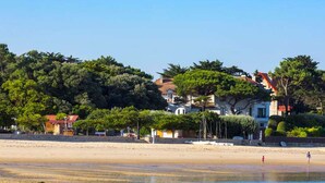 Une plage avec un rivage sablonneux, quelques personnes et, au loin, des bâtiments aux toits rouges.