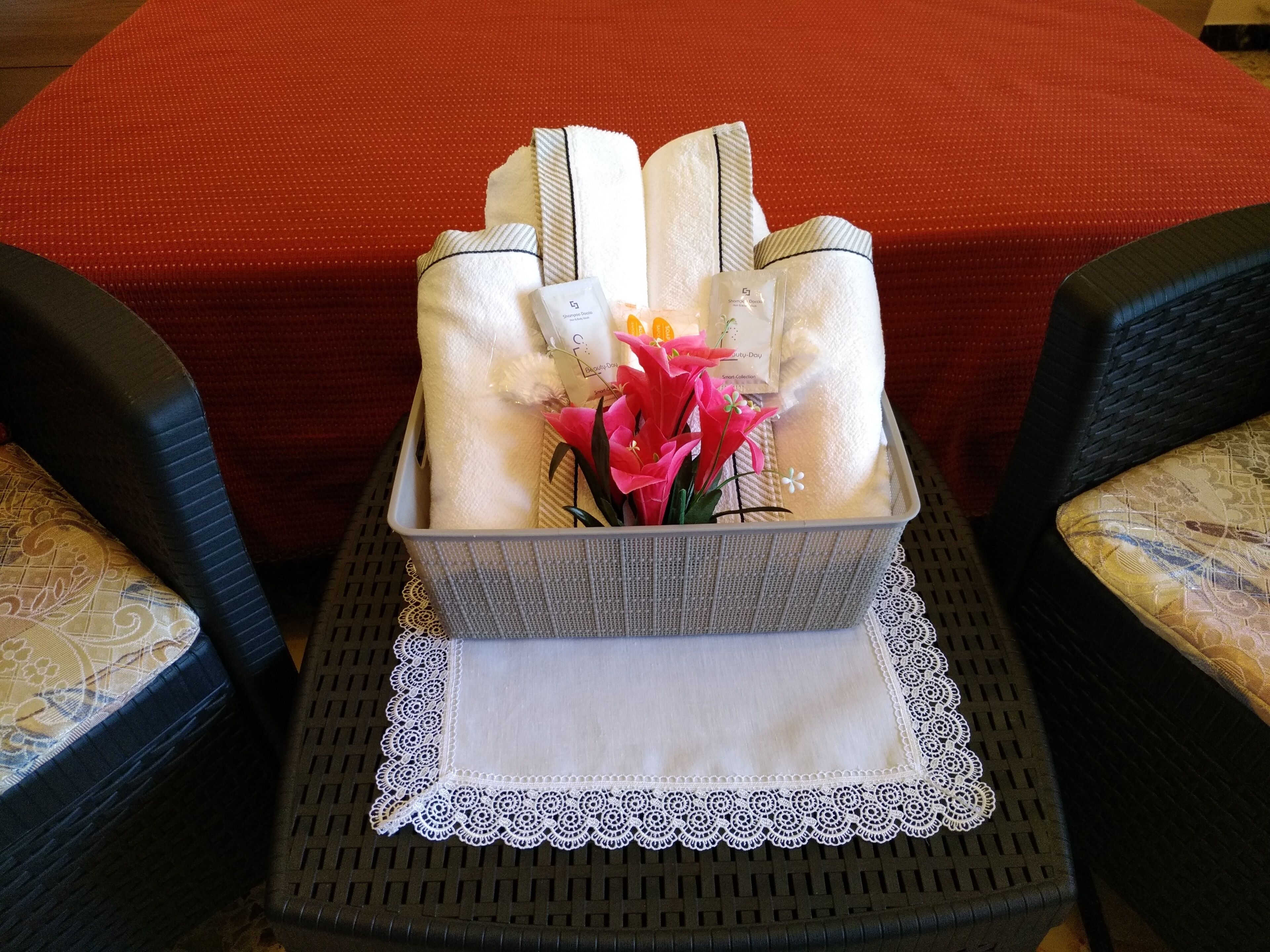 Un plateau avec des serviettes pliées, un petit vase avec des fleurs et une boîte de mouchoirs sur une table recouverte d’une nappe en dentelle.