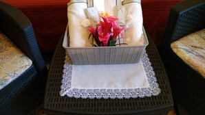 Una bandeja con toallas dobladas, un pequeño jarrón con flores y una caja de pañuelos sobre una mesa con un mantel de encaje.