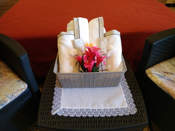 Una bandeja con toallas dobladas, un pequeño jarrón con flores y una caja de pañuelos sobre una mesa con un mantel de encaje.
