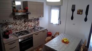 Cocina compacta con estufa a gas, horno y lavaplatos. Hay una mesa de comedor con sillas y un frutero.