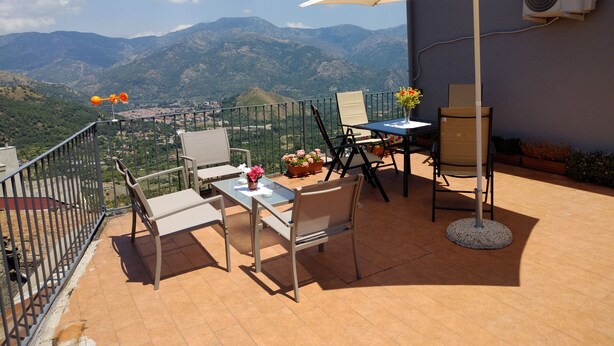 Una terraza con una mesa, sillas, un paraguas blanco y vistas a las montañas.