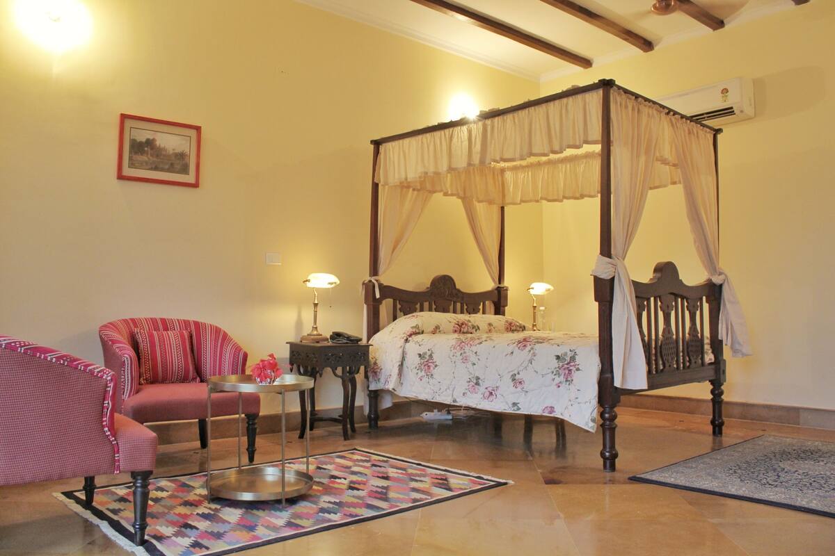 A bedroom with a four-poster bed, a chair, a small table, and a rug.