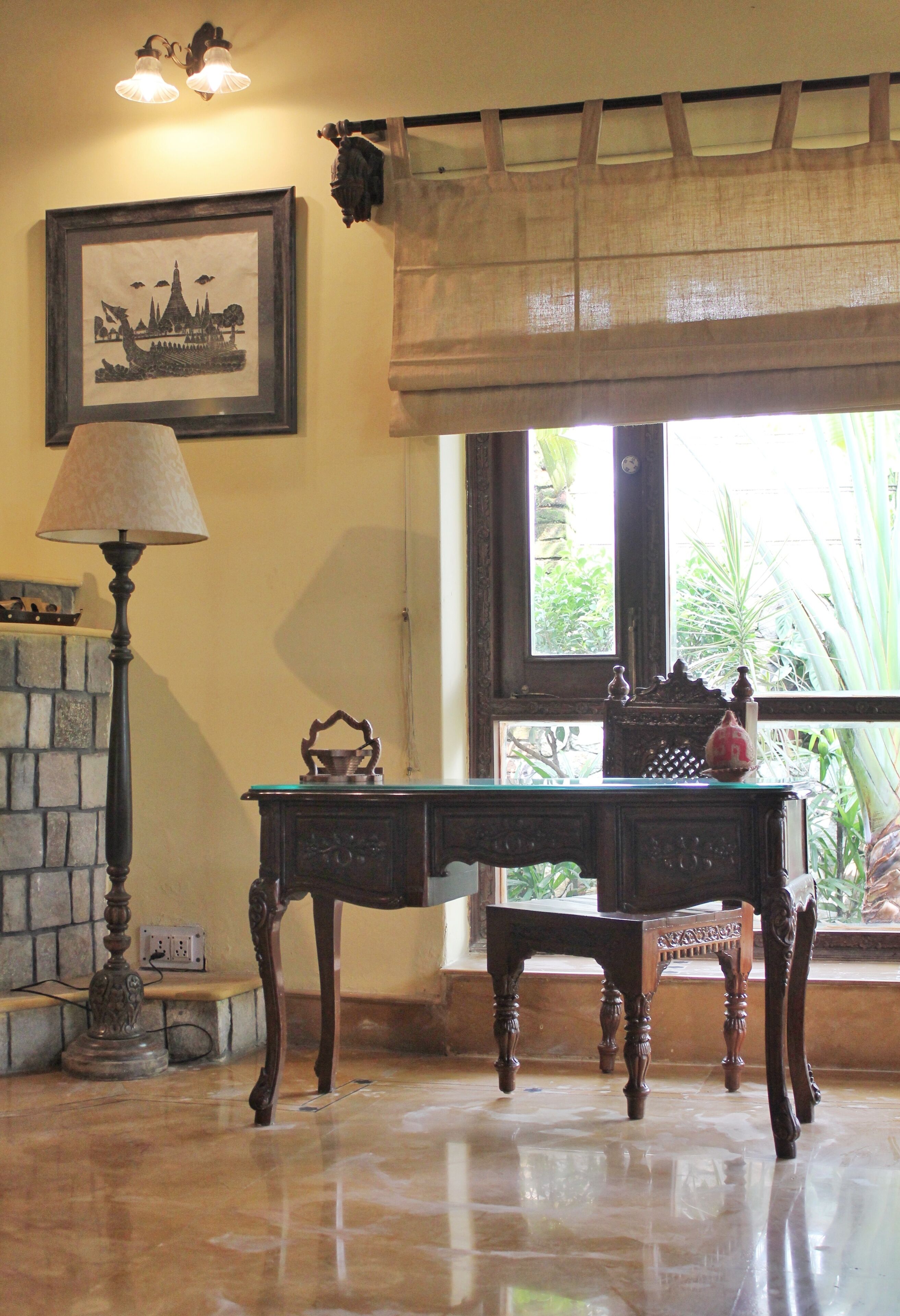 Una habitación con un escritorio de madera, una lámpara, un cuadro en la pared y una ventana con vistas a la vegetación.