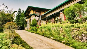 A traditional stone building with a green roof, surrounded by lush greenery and a stone wall. - Tree of Life Resort, Dehradun Foothills (Dehradun)