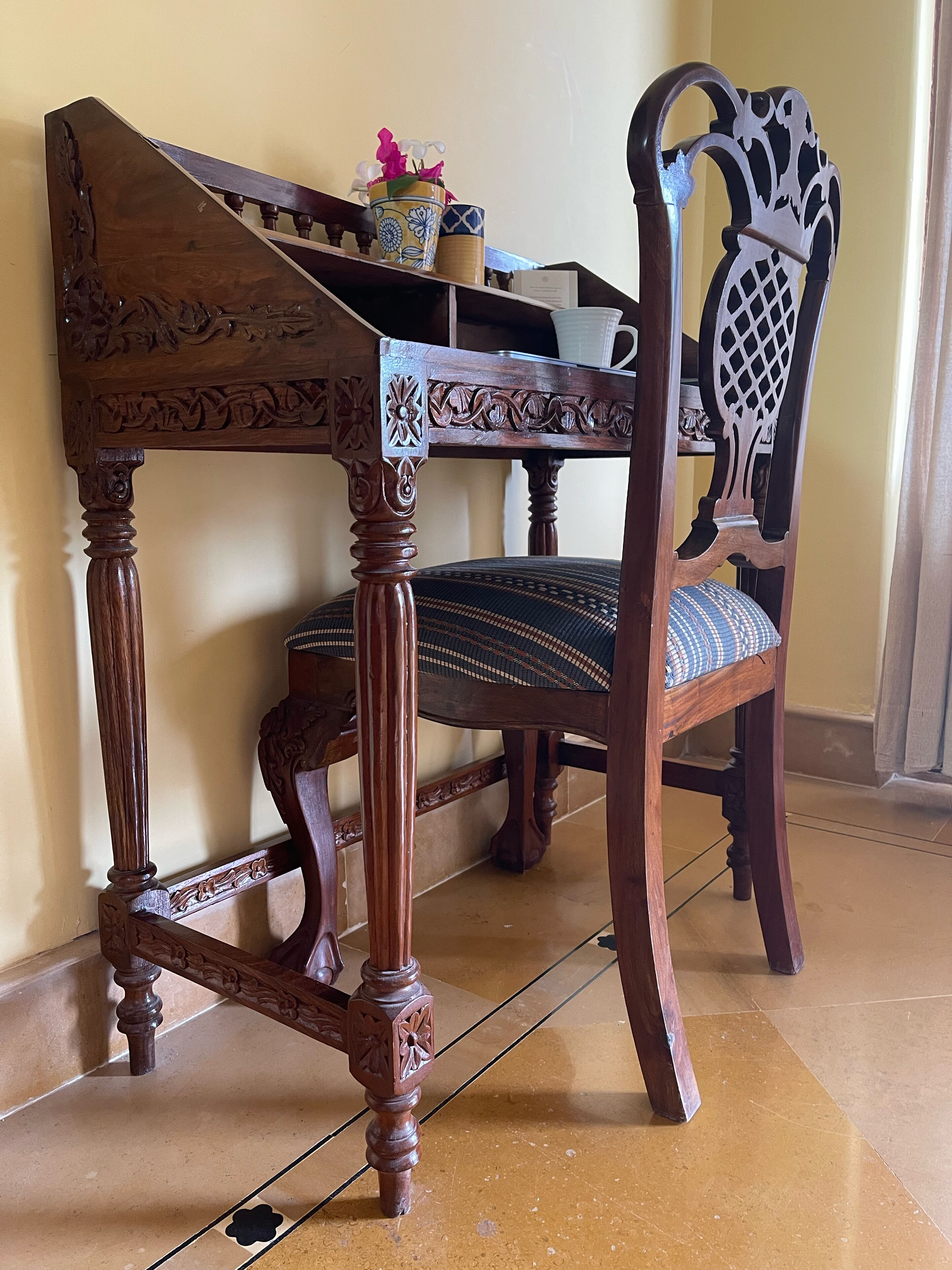 A wooden chair with intricate carvings and a woven seat, placed next to a table with a potted plant.