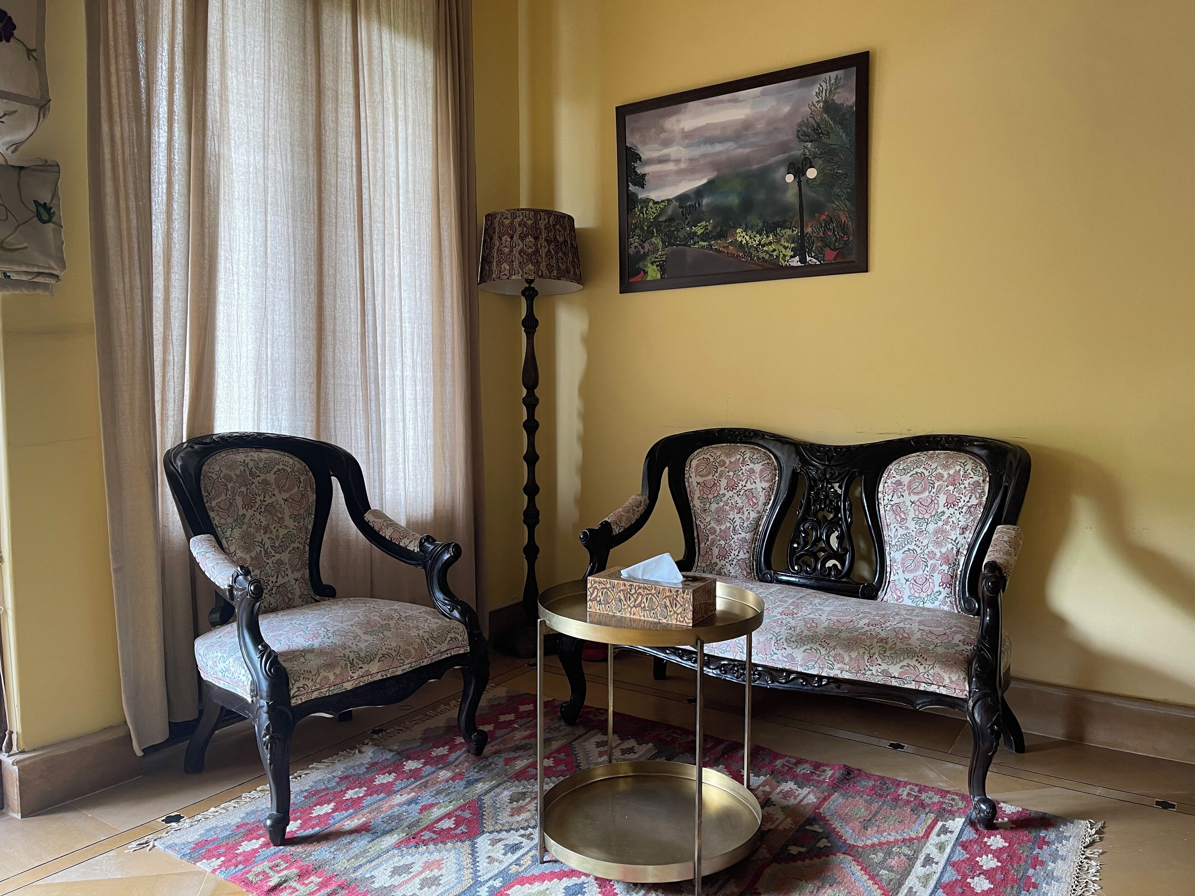 Ein Zimmer mit einer Couch, zwei Sesseln, einem kleinen Tisch mit Tablett, einer Lampe und einem Bild an der Wand.