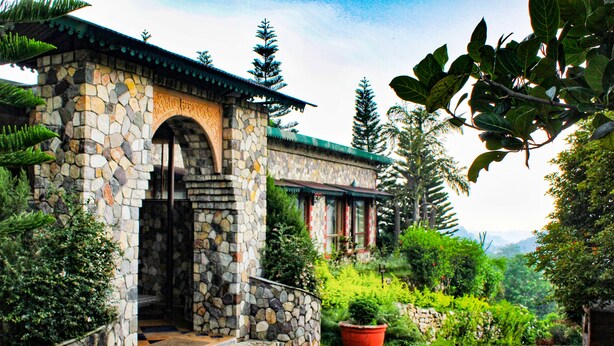 A stone building with a stone staircase leading to an entrance, surrounded by lush greenery and a mountain backdrop. - Tree of Life Resort, Dehradun Foothills (Dehradun)
